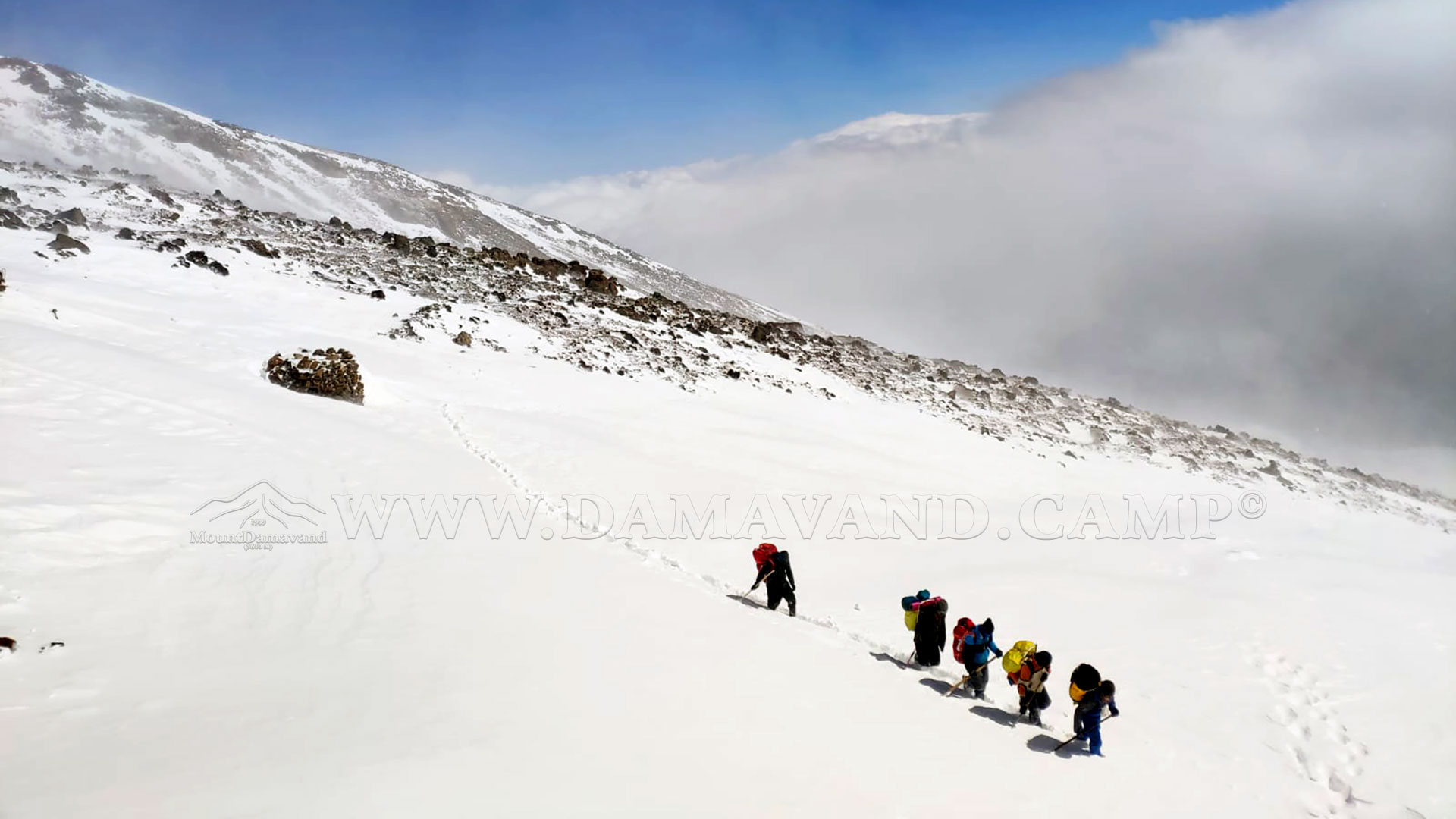 Hardworking porters are carrying duffel bags on a snow-covered slope to the camp.